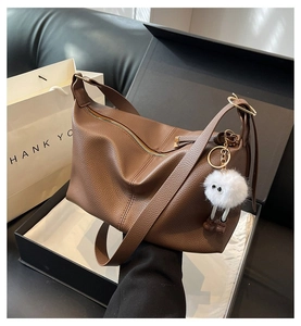 Close-up of brown litchi pattern leather tote bag with gold zipper and white plush charm