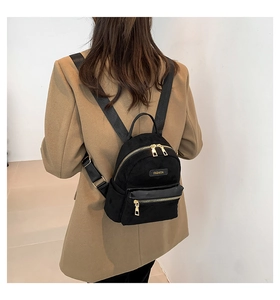 Détail d'un mini sac à dos noir avec fermetures dorées sur un mannequin en manteau