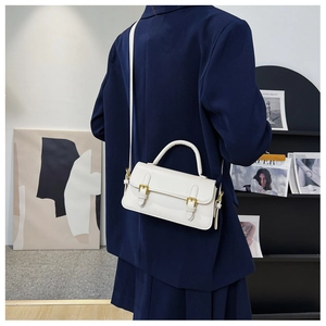 White glossy leather flap bag with gold buckles worn over a navy blue blazer