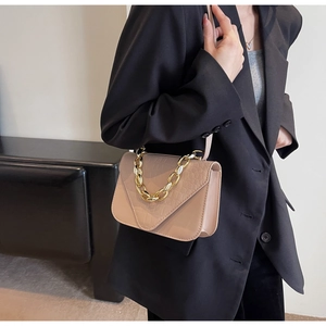 Close-up of beige stone-embossed crossbody bag with thick gold chain handle on model