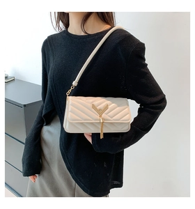 Detail of cream quilted crossbody bag with golden V-shaped metal buckle and tassel