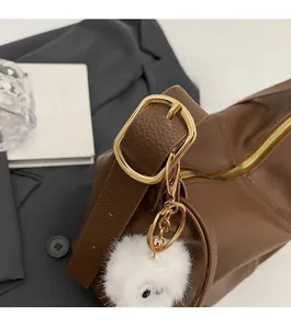 Detail of dark brown pebble leather tote bag with gold metal buckle and plush ball charm