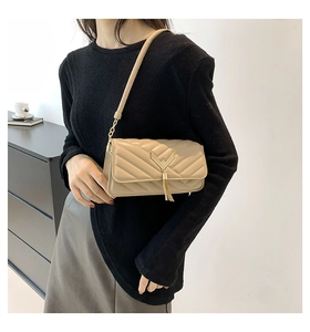 Detail of beige quilted shoulder bag with golden V-clasp and metallic tassel accent
