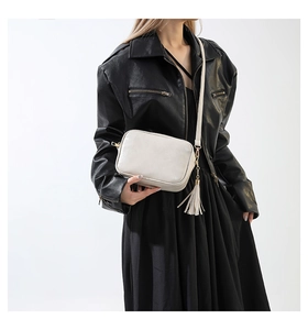 Detail of a creamy white crossbody bag featuring golden zippers and stylish long tassels