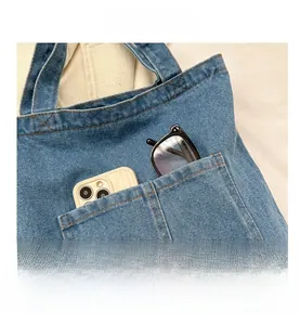 Detail view of denim tote bag pocket holding a gold smartphone and black glasses