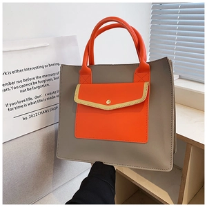 Detail of grey tote bag with orange handle and gold buckle on a stylish wooden desk