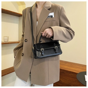 Detail of black matte leather crossbody bag with gold buckles styled on a vintage suit
