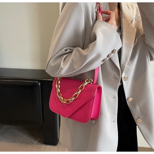 Detail of fuchsia crocodile pattern crossbody bag with chunky gold chain on grey blazer