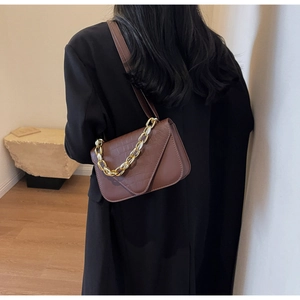 Close-up of brown crocodile texture bag with gold chain strap in a minimal setting