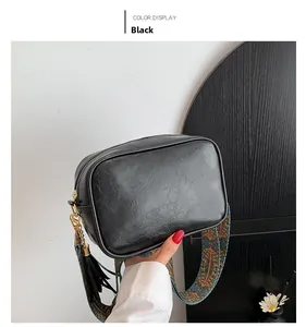 Detail of black crossbody bag with vintage woven strap and tassel charm held by model