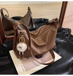 Close-up of brown litchi pattern leather underarm bag with cute white plush ball charm