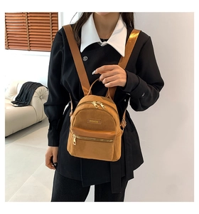 Détail d'un mini sac à dos carré en daim fauve avec logo doré porté par un mannequin