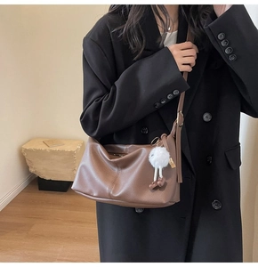 Close-up of brown pebbled leather crescent bag with a white plush doll charm detail