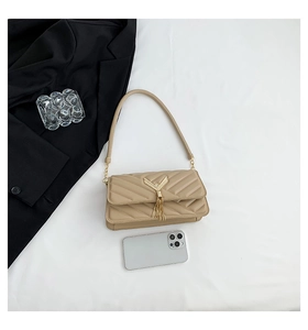 Close-up of quilted shoulder bag with gold V-hardware, tassel, and smartphone for size scale