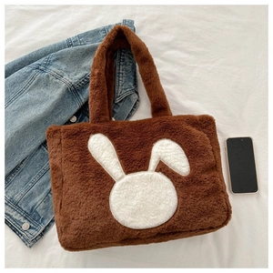 Détail d'un sac cabas pelucheux marron avec broderie lapin sur un tissu blanc