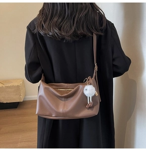 Detail view of brown pebbled leather tote bag with white plush charm and gold hardware