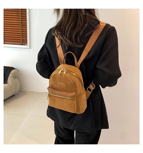 Gros plan d'un mini sac à dos en daim marron avec plaque en métal et détails zippés