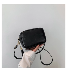 Detail of black crossbody camera bag featuring glossy PU leather and a decorative tassel fringe
