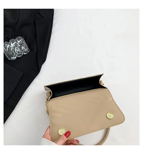 Detail of beige flap handbag showing dual gold magnetic buckles and black inner lining