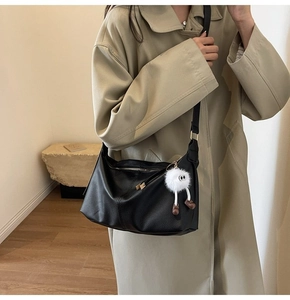 Detail of black pebble leather tote bag with cute white plush monster charm accessory