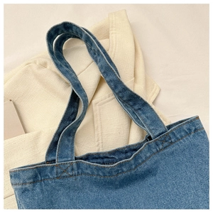 Close-up of blue denim tote bag upper with yellow stitching and sturdy handles