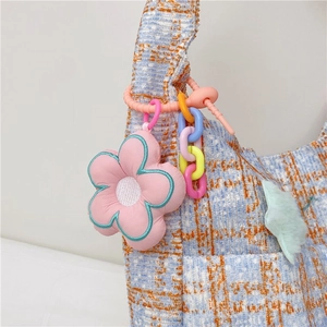Nahaufnahme der blau-orangen Tweed-Tasche mit rosa Blumenanhänger und bunter Kette
