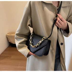 Detail view of black crocodile pattern crossbody bag with gold chain strap worn by a model