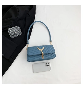 Close-up of quilted blue shoulder bag with golden V-shaped tassel and size comparison