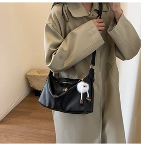 Detail of minimalist black textured leather tote bag with creative white plush charm