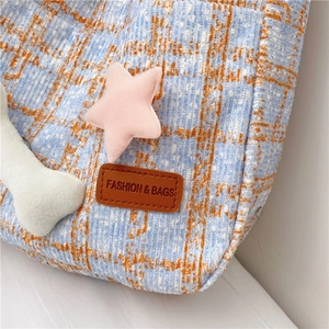 Detail der Cord-Textur, Karomuster und süße Plüschstern-Anhänger an der Handtasche