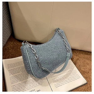 Détail du sac hobo en polaire bleue avec chaîne argentée sur canapé cuir