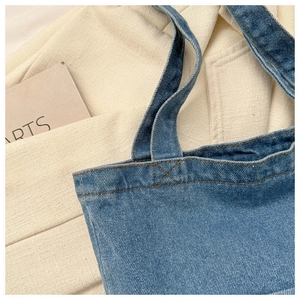 Detail of light blue denim tote bag showing stitching and handle quality on white fabric