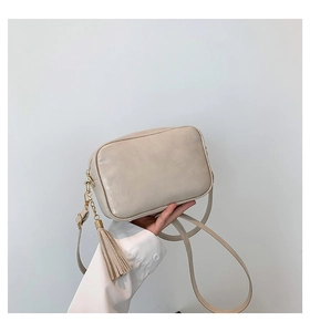 Detailed view of beige crossbody bag texture featuring elegant side tassel and strap
