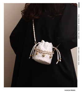 Detail of white quilted drawstring bucket bag with gold heart charms and chain strap