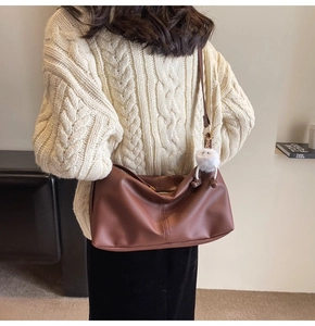 Brown litchi grain leather tote bag with pompom charm shown on shoulder with a cozy sweater
