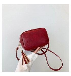 Detail view of red vintage crossbody bag with soft leather texture and long tassel charm