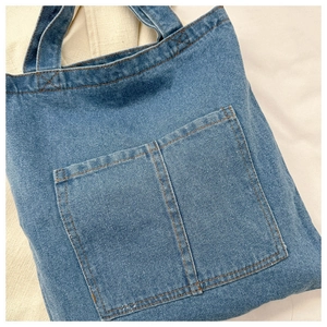 Detailed view of blue denim tote bag with large front pockets and yellow stitching detail