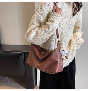 Detail of brown pebbled leather hobo bag with cute white plush charm on a model