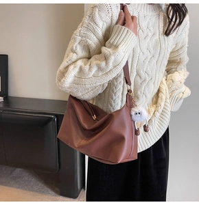 Close-up of brown pebbled leather tote bag with a cute white plush monster charm
