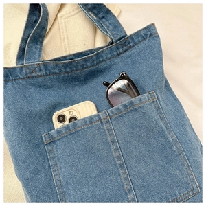 Detail view of denim tote bag showing front double pockets with phone and sunglasses