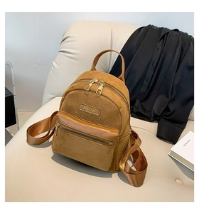 Détail d'un mini sac à dos en daim marron avec plaque fashion sur fond en cuir beige