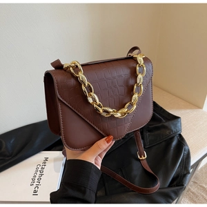Detail showing deep brown crocodile pattern leather and bold gold metal chain on bag