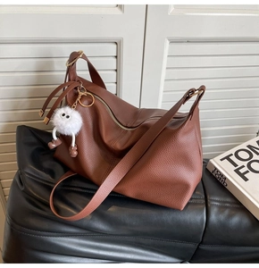 Detail of brown litchi leather tote bag with furry monster charm on dark cushion