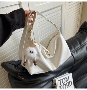 Detail of white lychee grain hobo bag with gold hardware and plush monster charm