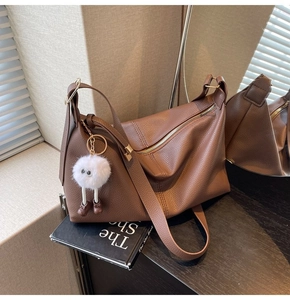 Detailed side view of a brown pebbled leather tote bag with a white plush charm