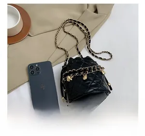 Detail showing quilted leather bucket bag with gold chain and heart charm beside a smartphone