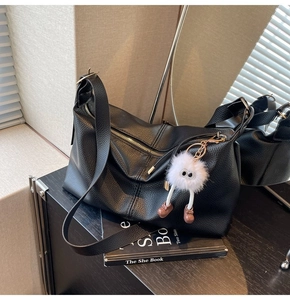 Close-up of black litchi grain leather tote bag with a cute monster plush pendant