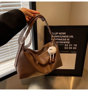 Detail of a brown lychee pattern leather hobo bag featuring a white plush charm and strap