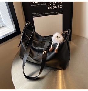 Close-up of black lychee leather tote bag with a white plush monster charm on a silver table