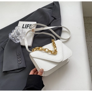 Detail of white faux leather crossbody bag with crocodile texture and gold chain strap